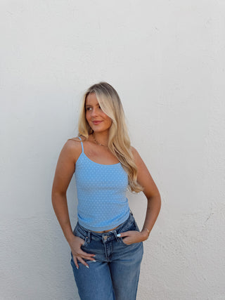Woman wearing a blue top and jeans against a white wall