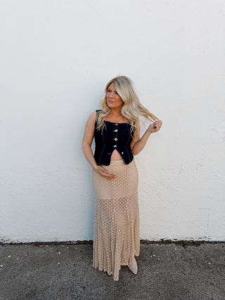 Woman in a black top and beige skirt standing on a white surface with a gray border.
