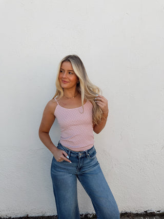 Woman wearing a pink top and blue jeans against a white wall