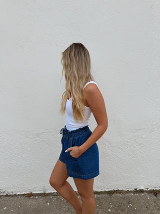 Woman modeling a white top and dark denim shorts