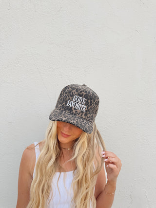 Woman modeling a leopard trucker hat with the saying "God's favorite" on it