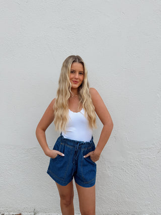 Woman modeling a white top and dark denim shorts