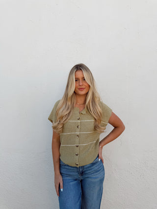 Woman wearing a green vest and blue jeans against a white background