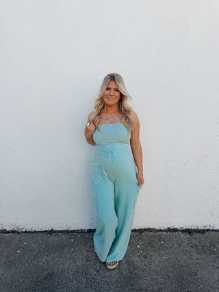 Woman in a light blue dress standing on a white wall and gray pavement.