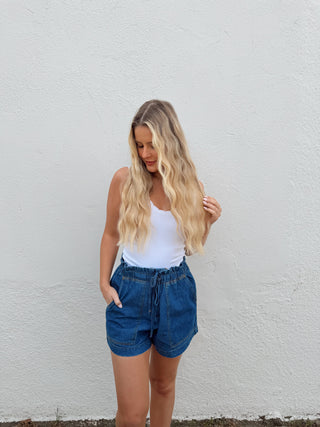 Woman modeling a white top and dark denim shorts