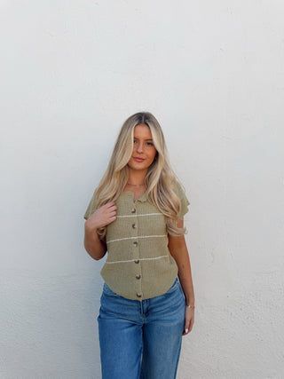 Woman wearing a green vest and blue jeans against a white background