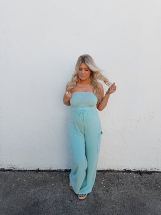 Person in a light blue outfit standing on a white wall and black pavement.