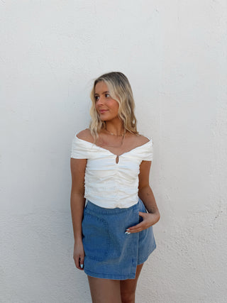 Woman wearing a white top and blue denim skirt against a plain background