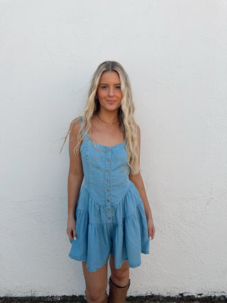 Woman in a blue romper standing against a white wall