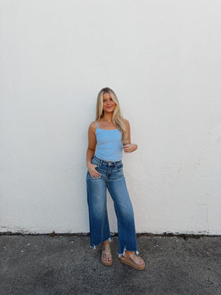 Person wearing a light blue top and jeans standing on a white and gray pavement.