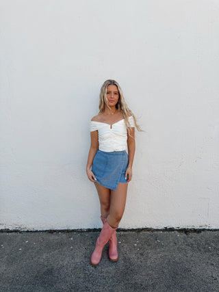 Person standing on a road with a white wall and gray pavement.