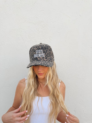 Woman modeling a leopard trucker hat with the saying "God's favorite" on it