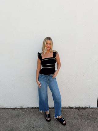 Woman modeling a black top with white detailing and jeans