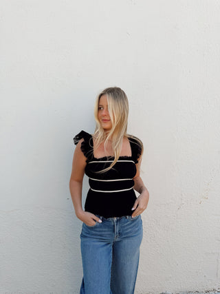 Woman modeling a black top with white detailing and jeans