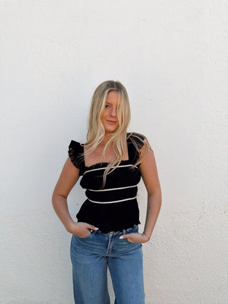 Woman modeling a black top with white detailing and jeans