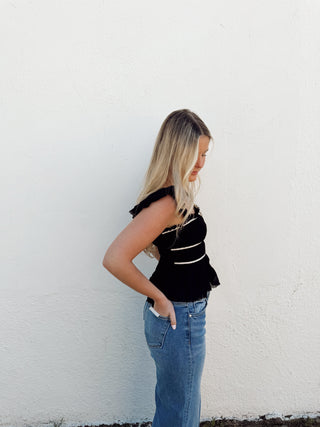 Woman modeling a black top with white detailing and jeans