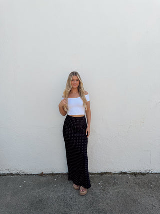 Person standing on a white wall with a black and white patterned skirt.